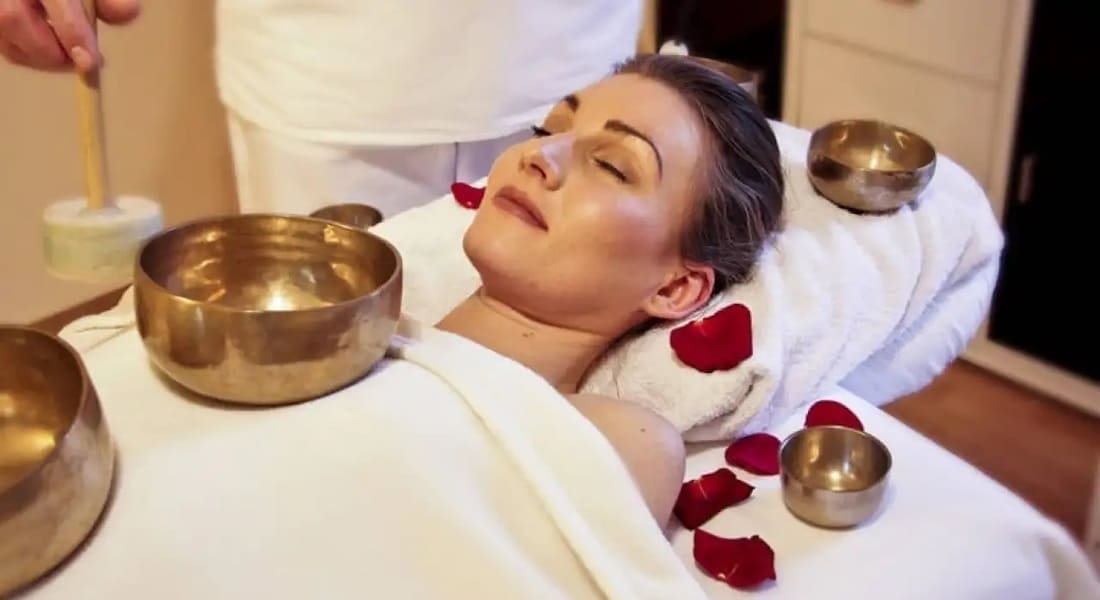 A smiling woman lying down getting a massage with several singing bowls