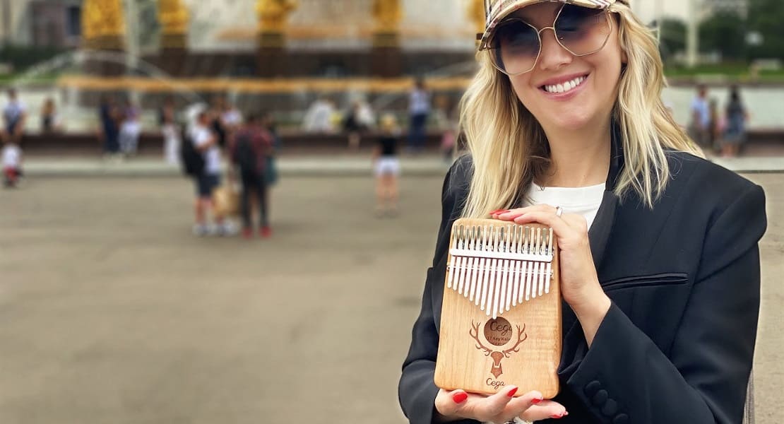 A smiling woman on the street wearing sunglasses holding a kalimba in her hands