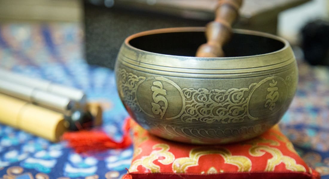 A metal-engraved Tibetan bowl on a gold and red fabric cushion.