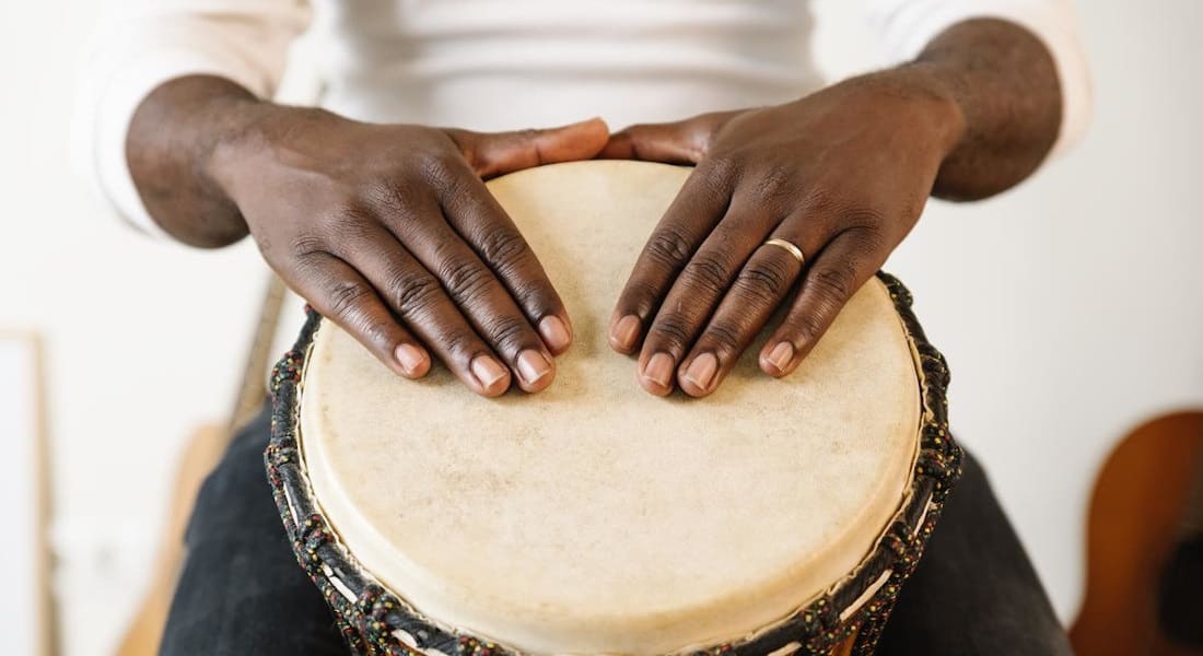 Two black hands resting on a white djembe