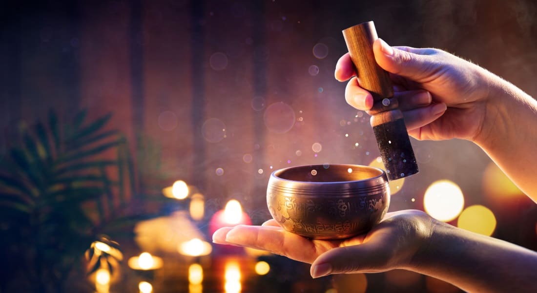 Two hands playing a Tibetan singing bowl surrounded by candles