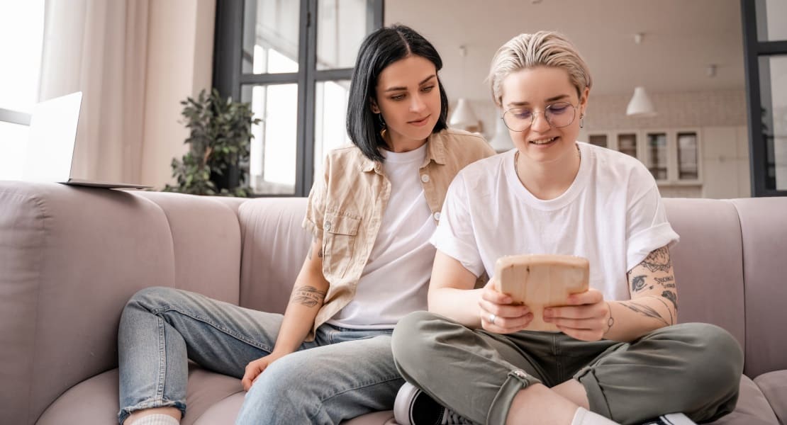 Two women sitting on a couch, one playing the kalimba