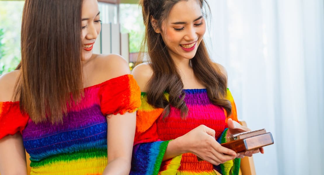 Two seated women, one smiling while playing the kalimba