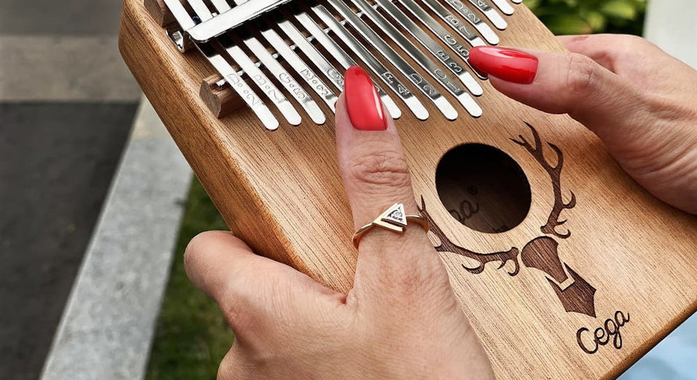 Two women's hands with red nails holding a Cega kalimba