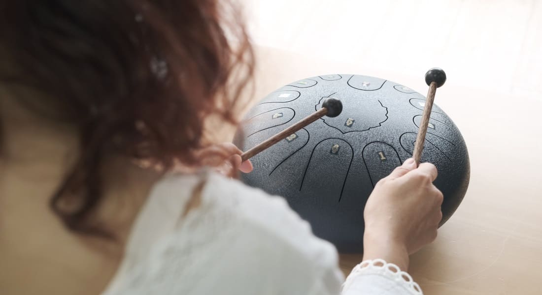 A woman seen from behind playing a tongue drum