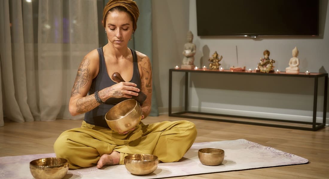 A woman sitting cross-legged in her living room holding a Tibetan singing bowl