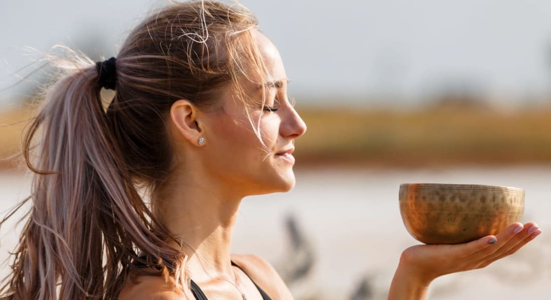 A woman with her eyes closed holding a singing bowl