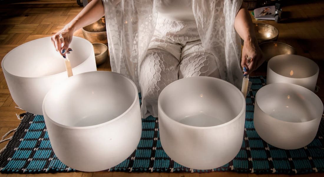 A woman kneeling while playing several crystal singing bowls