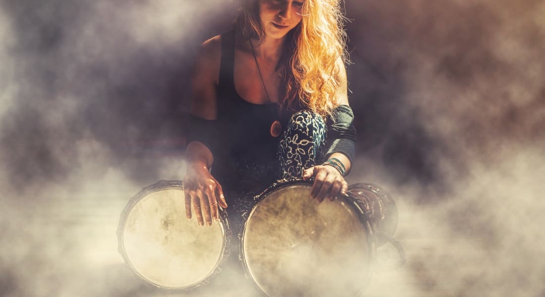 A woman kneeling with two djembes