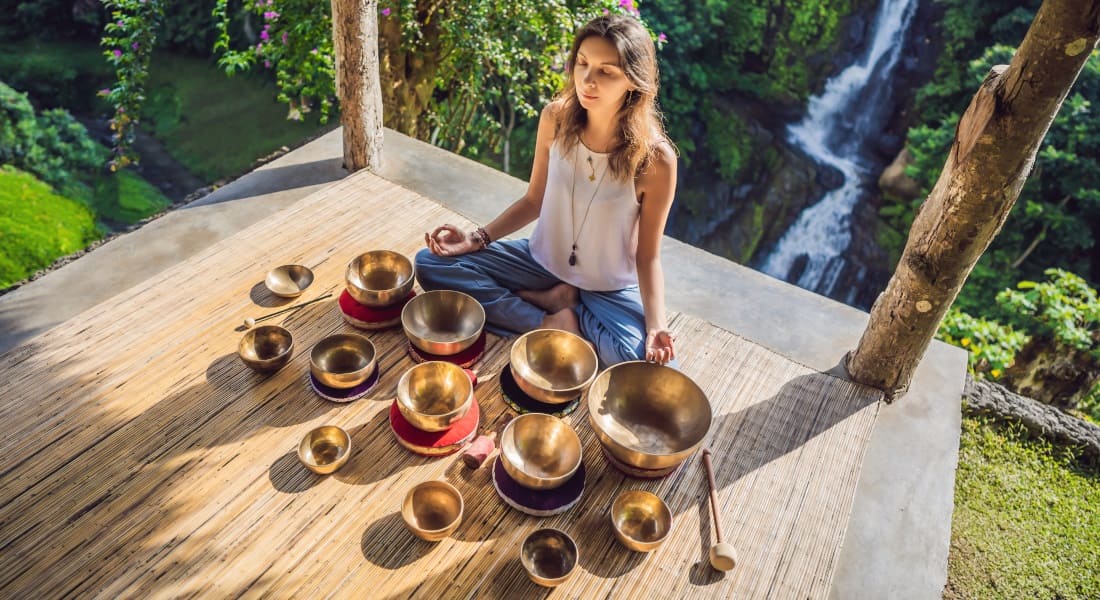 A woman seen from a low angle surrounded by Tibetan singing bowls