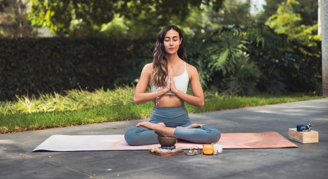 A woman meditating cross-legged with a metal singing bowl