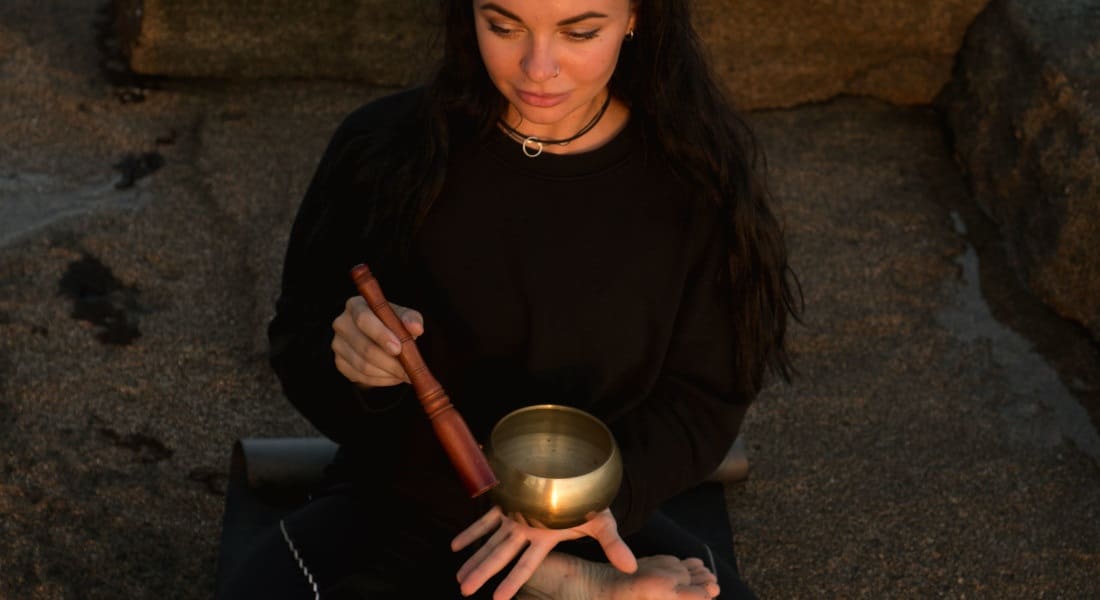 Woman meditating on the beach with a singing bowl