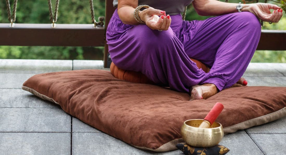 A woman meditating on a cushion with a Tibetan singing bowl
