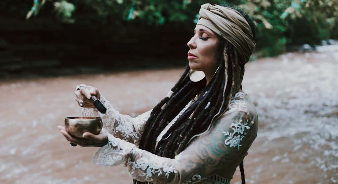 A woman near a river playing a Tibetan singing bowl