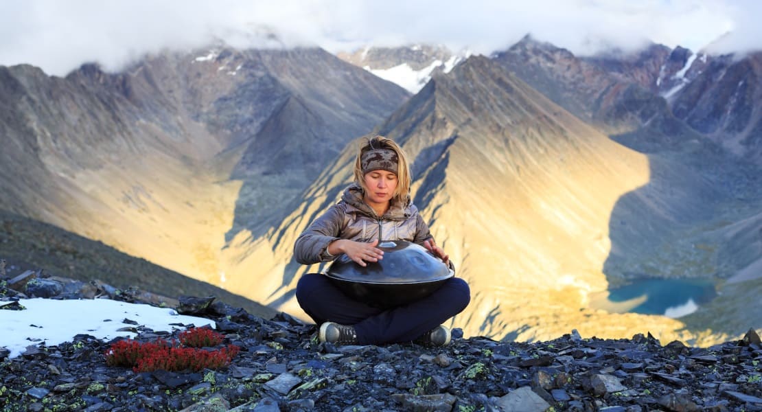 A woman playing a handpan in the mountains