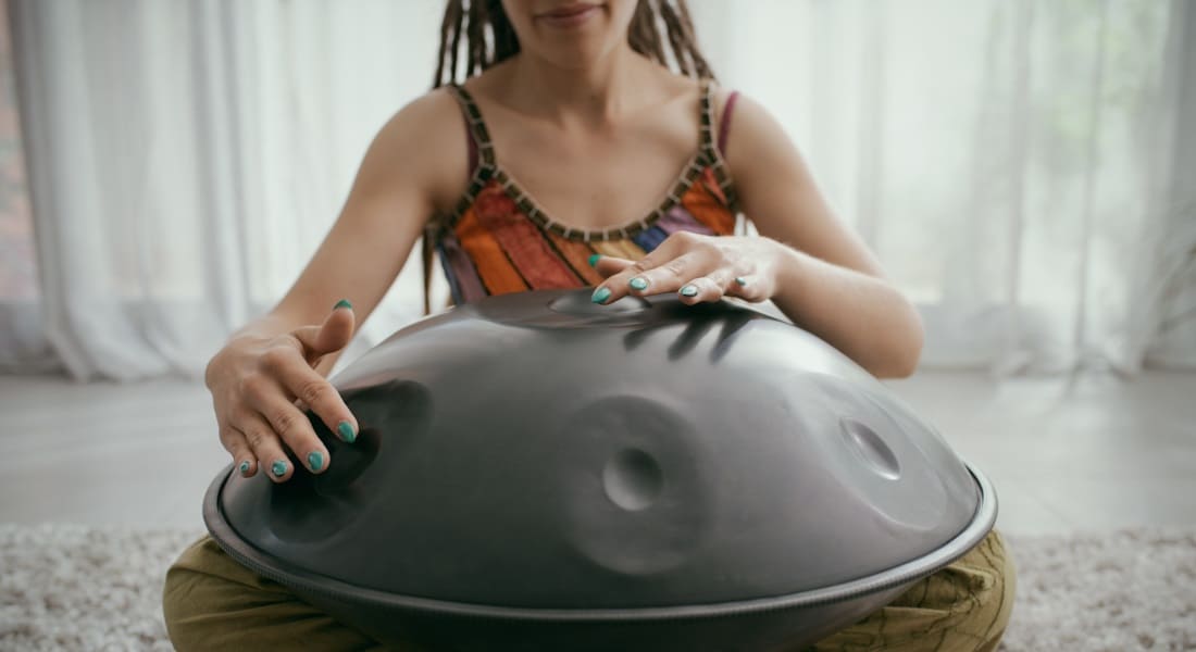 A woman playing while seated with a Hang