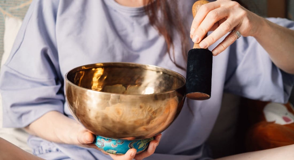A woman playing a Tibetan singing bowl on a blue cushion