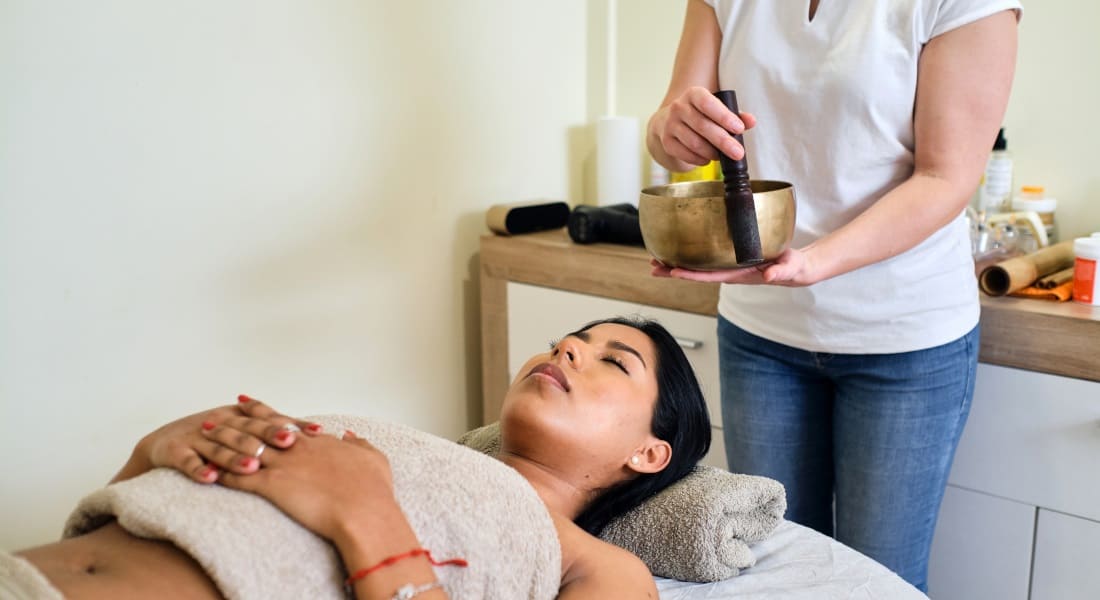 A woman lying down receiving a Tibetan singing bowl treatment