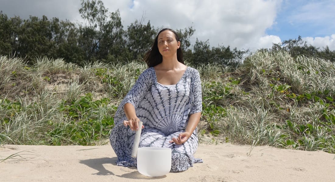 A woman on sand with a crystal Tibetan bowl