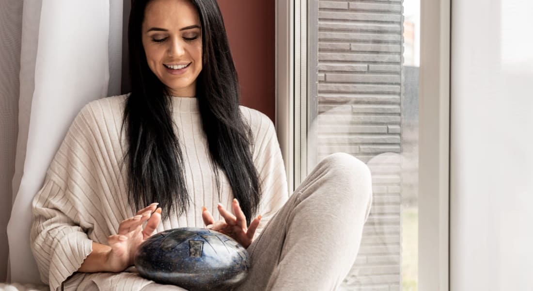 A woman sitting on a couch playing a hank drum