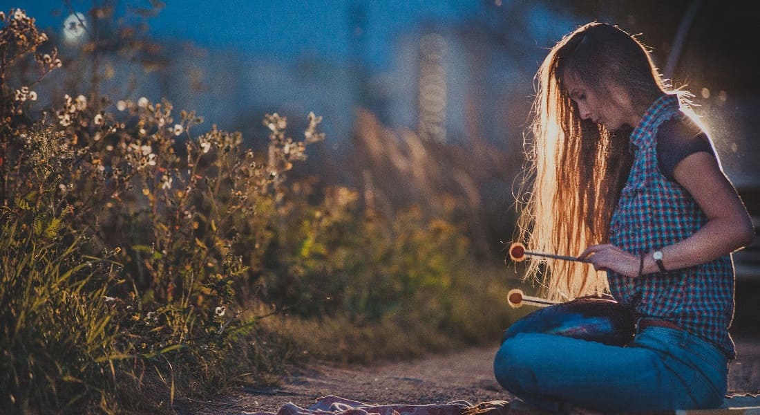 A woman sitting cross-legged on the floor with a tongue drum at night