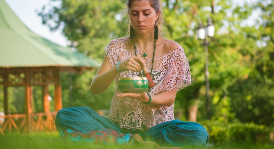 A woman sitting in the grass meditating with a singing bowl