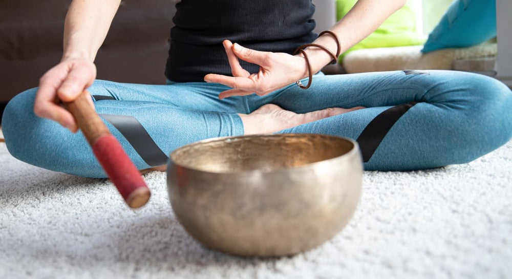A woman sitting in lotus pose meditating with a Tibetan singing bowl