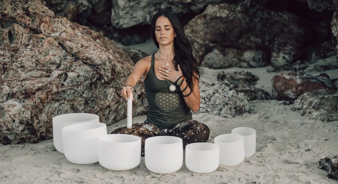 A woman sitting on a beach surrounded by 7 quartz bowls