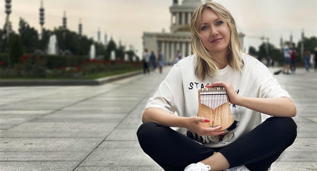 A woman sitting on the ground in a square holding a kalimba in her hands