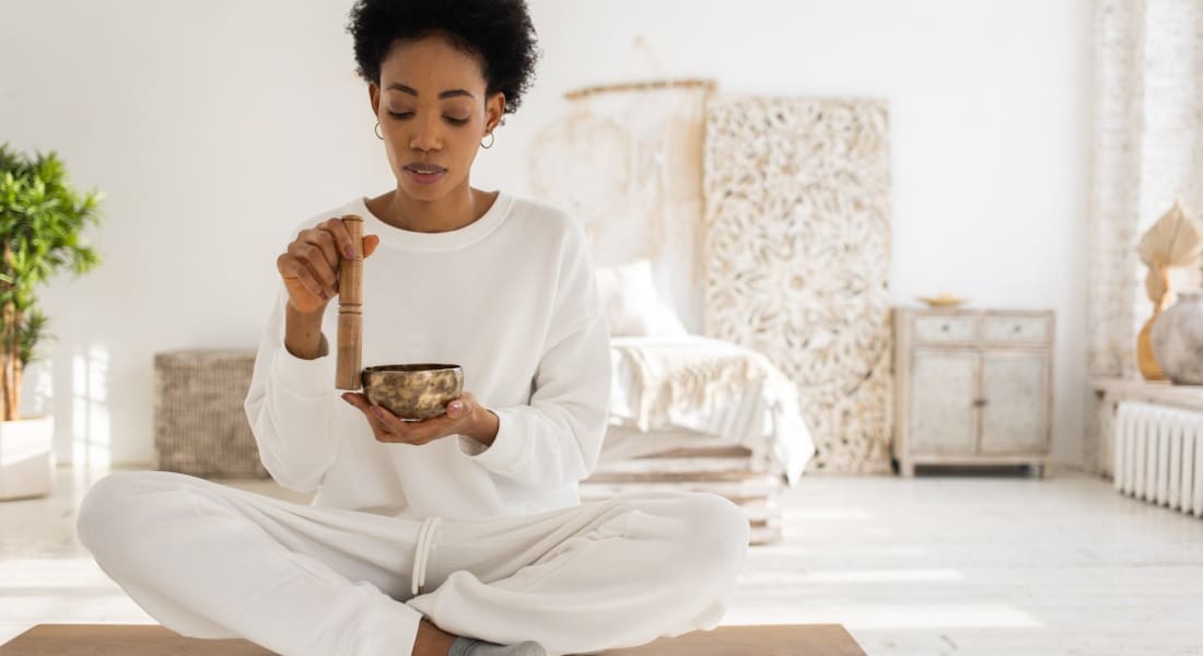 A woman sitting on a table playing a Tibetan singing bowl