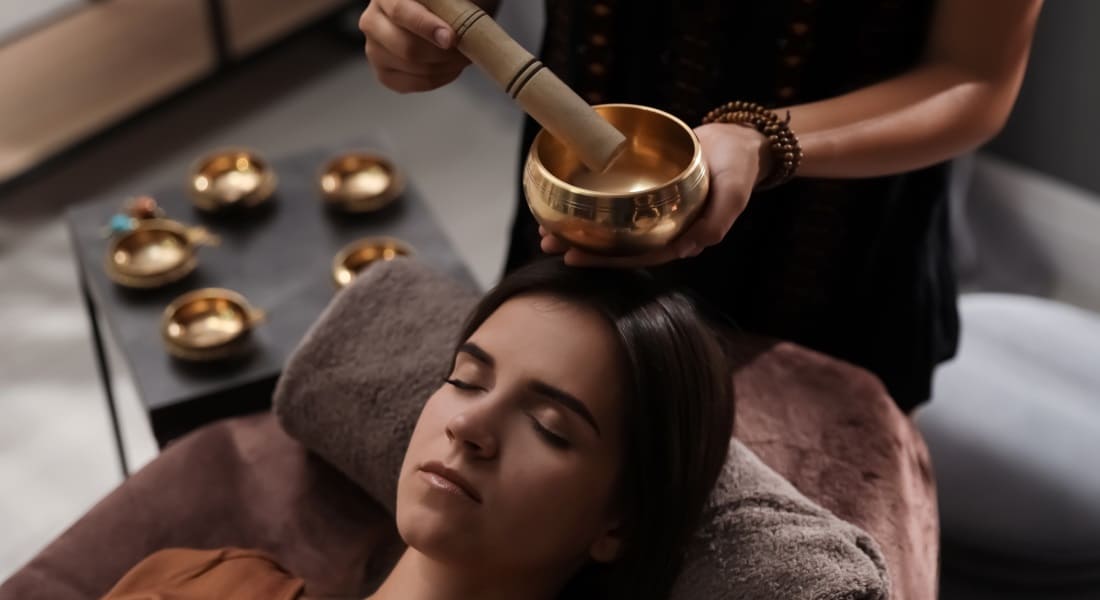 A woman lying down enjoying a sound massage with a small Tibetan singing bowl
