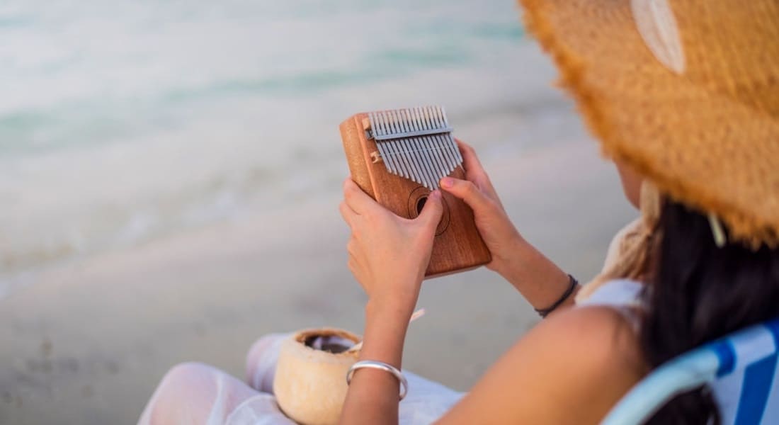 Woman wearing a straw hat seen from behind playing a kalimba