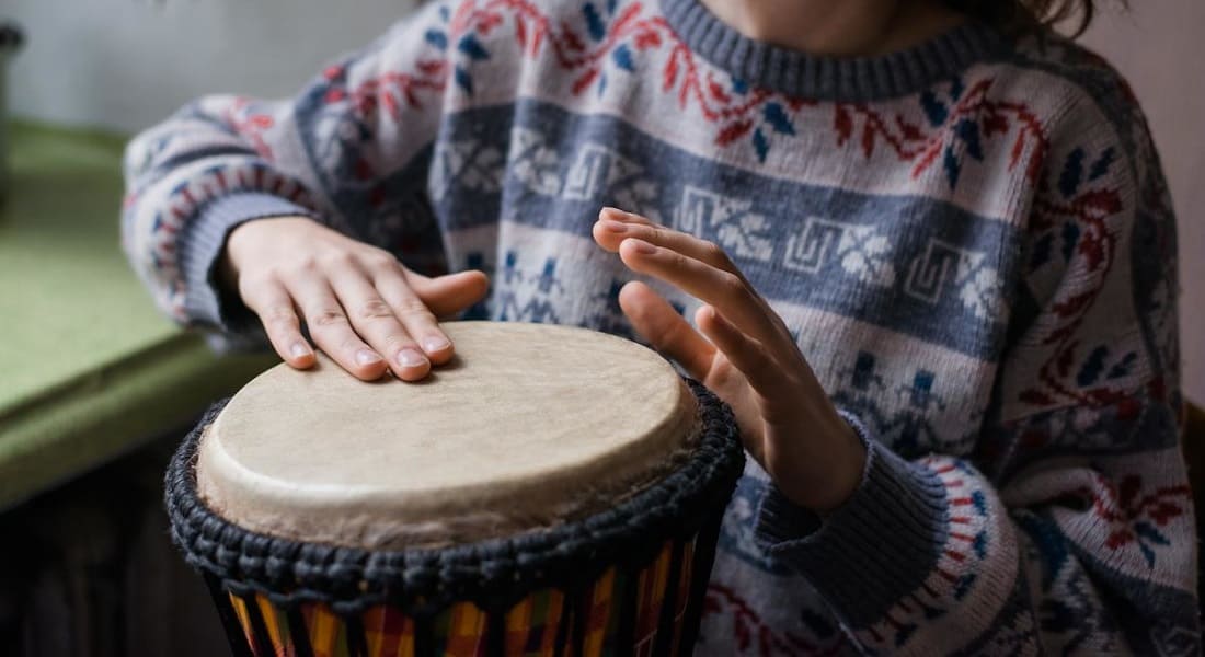 A woman in a sweater playing a small djembe