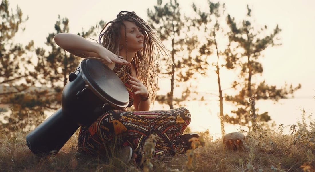 A woman with dreadlocks playing a djembe