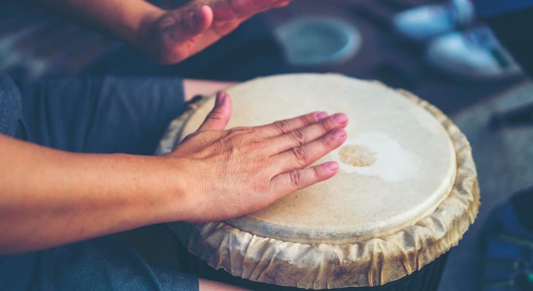 Close-up of two hands striking a djembe drumhead